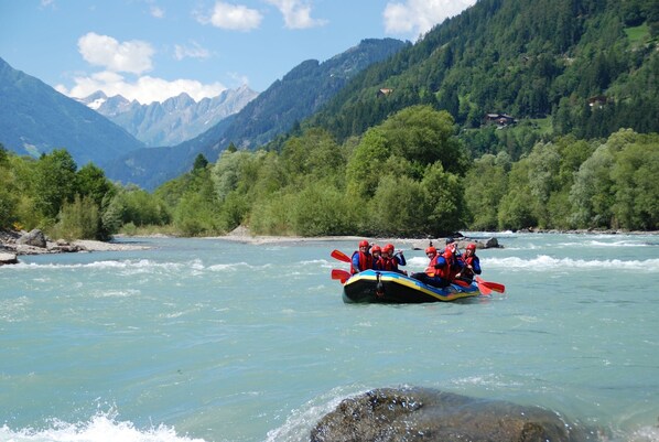 Un groupe de personnes fait du rafting sur une rivière, entourée de montagnes.