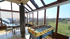 A spacious room with a foosball table, a dining table, and chairs, with large windows offering a view of the outdoors. - Holiday Home in Noiseux With BBQ Terrace (Somme-Leuze)