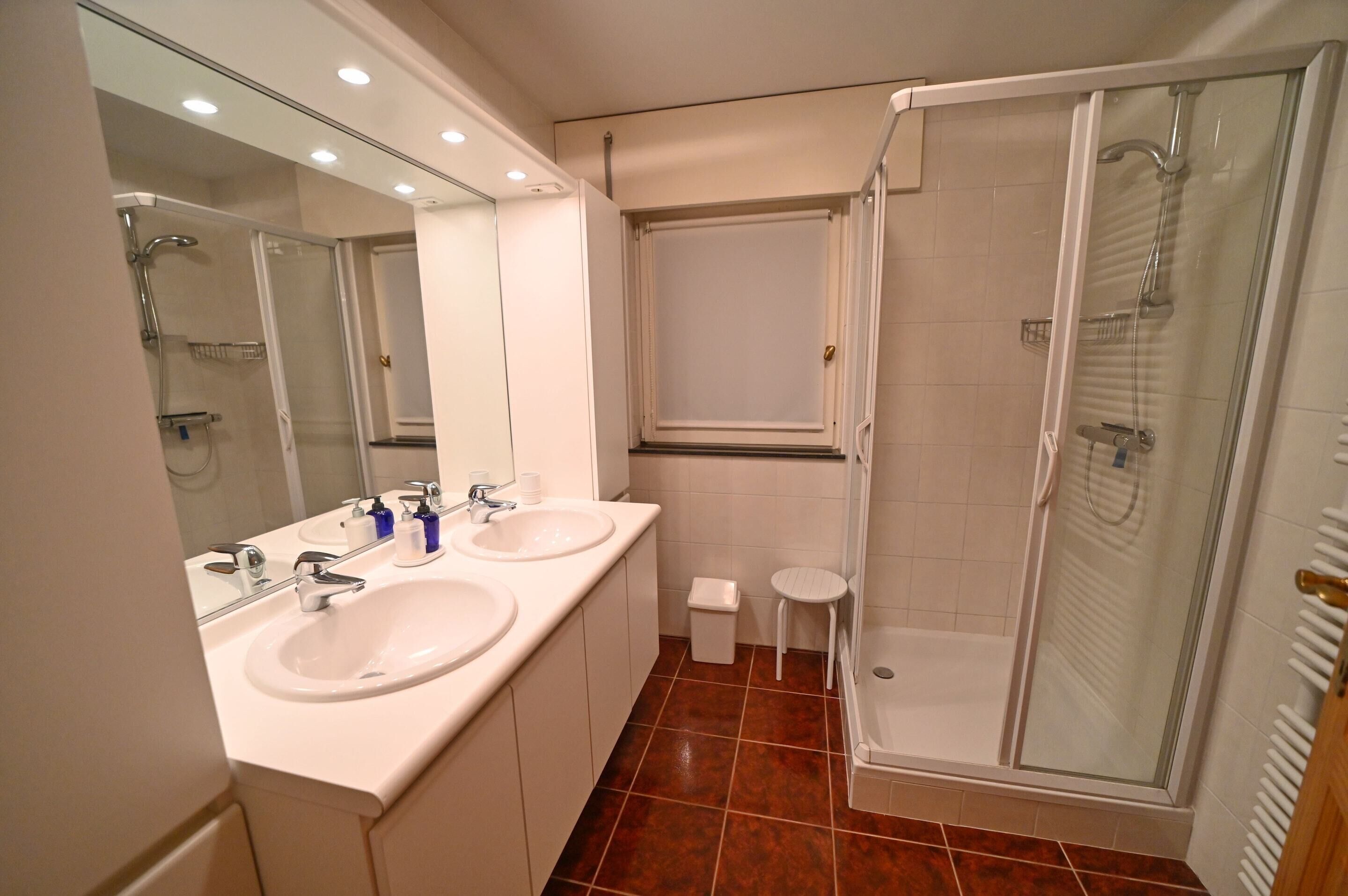 A bathroom with two sinks, a mirror, a shower, and a toilet.