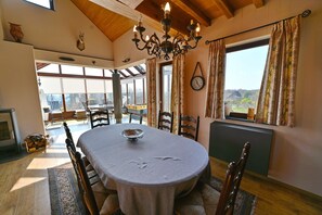 A dining room with a round table, chairs, a chandelier, and a view through large windows. - Holiday Home in Noiseux With BBQ Terrace (Somme-Leuze)