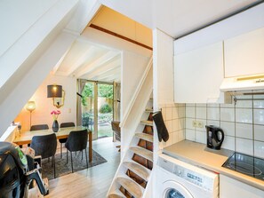 A modern kitchen with a built-in washing machine, a dining area with a table and chairs, and a staircase leading to a balcony with a view of the outdoors. - Welcoming Chalet in Rekem Tucked in Nature (Lanaken)