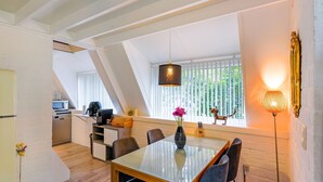 A modern dining area with a glass table, dark chairs, and a vase of flowers. A kitchen is visible in the background with a microwave and coffee maker. - Welcoming Chalet in Rekem Tucked in Nature (Lanaken)