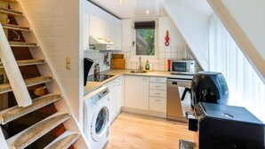 A compact kitchen with a washing machine, microwave, and a coffee machine. - Welcoming Chalet in Rekem Tucked in Nature (Lanaken)