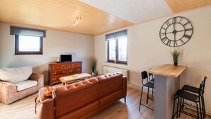 A spacious living area with a brown leather sofa, a wooden coffee table, a TV on a wooden cabinet, and a wall clock. - Holiday Home in Leglise With Garden (Léglise)
