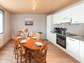 Une cuisine moderne avec des meubles blancs, un four noir et un coin repas comprenant une table et des chaises en bois.