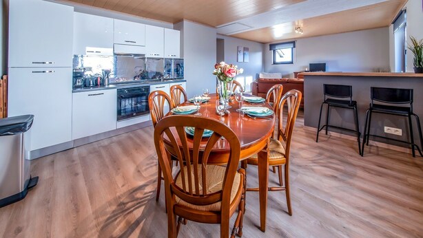 A modern kitchen with white cabinets, a wooden dining table with chairs, and a central vase with flowers. - Holiday Home in Leglise With Garden (Léglise)
