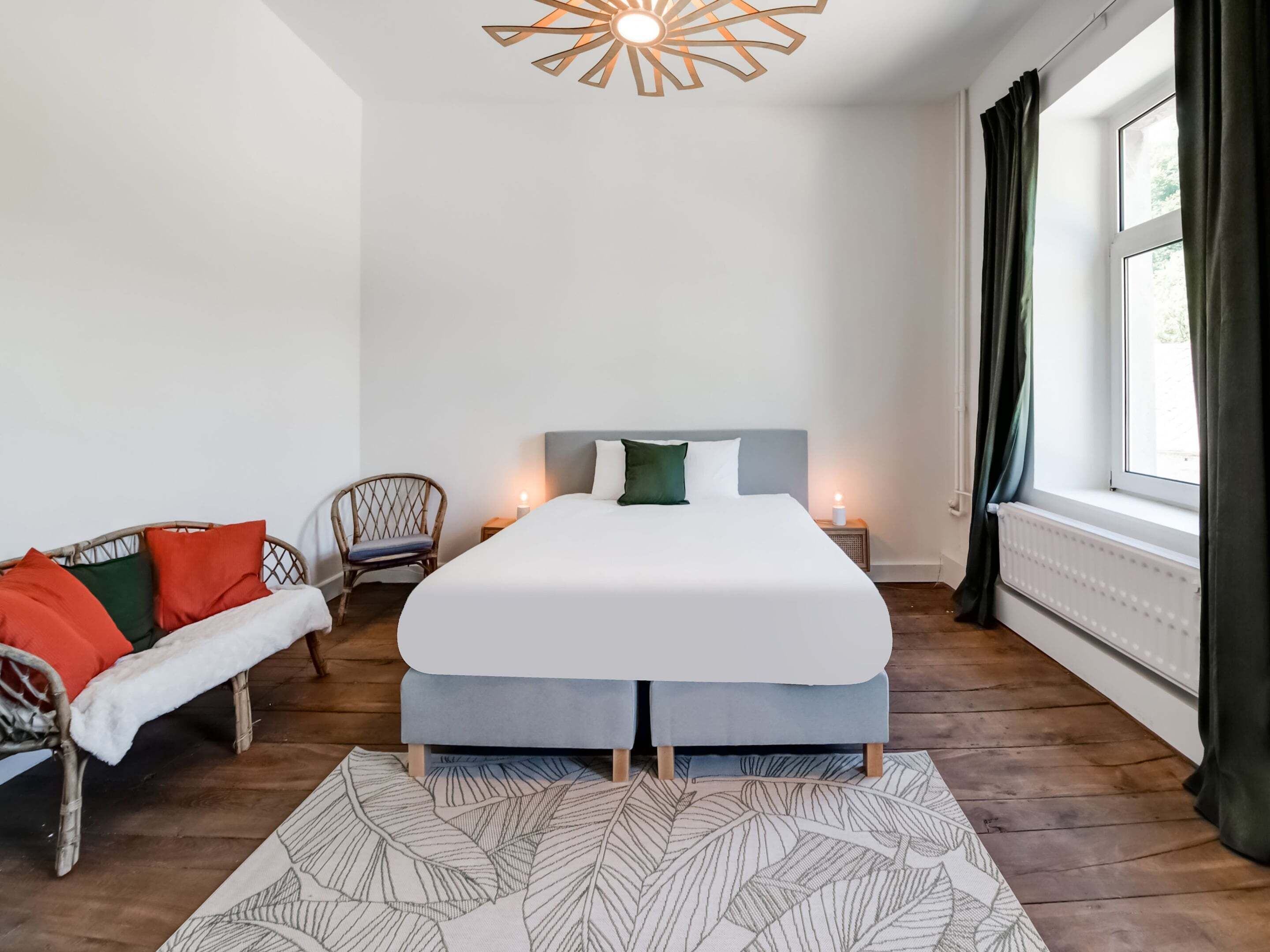 Une chambre à coucher avec un lit, une chaise, une petite table, une lampe sur pied et une fenêtre avec des rideaux.