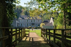 A stone building with a wooden bridge leading to it, surrounded by trees and greenery. - Castle in Ferrieres With Pond Garden (Ferrieres)