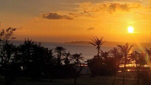 A sunset over a beach with palm trees and a distant island. - Enjoy kenting (Hengchun)