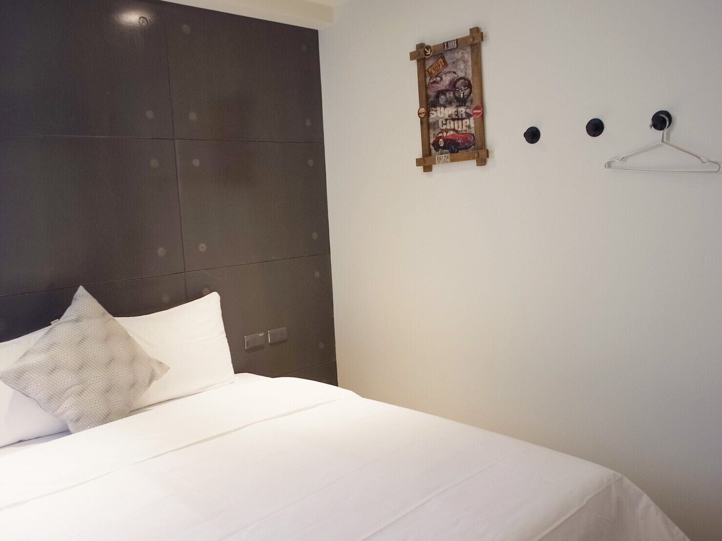 Ein Hotelzimmer mit einem großen Bett, einem Kopfteil, einem an der Wand befestigten Poster und einem Kleiderhaken.