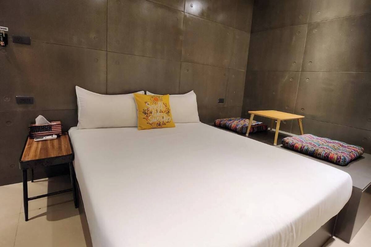 A modern hotel room with a large bed, a small wooden side table, and a nightstand.