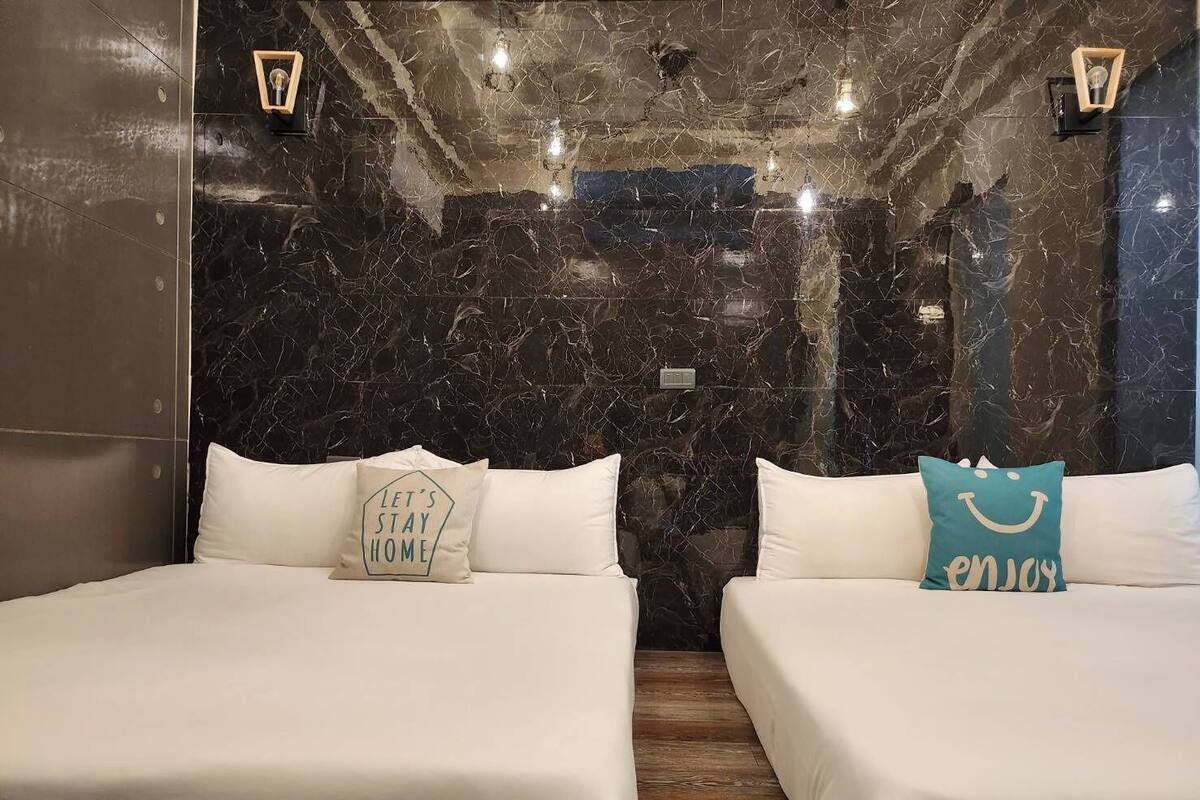 A hotel room with two beds, marble walls, and wall-mounted lights.