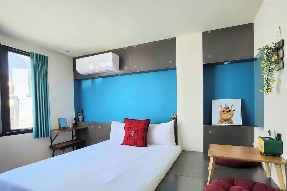 A modern hotel room with a large bed, a desk, a small seating area, and a window with curtains.