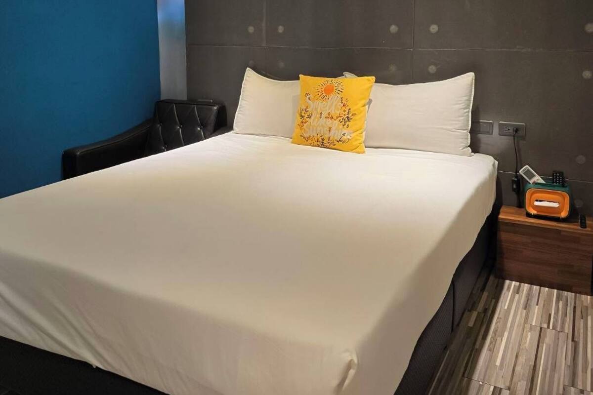 A modern hotel room with a large bed, a nightstand with a radio, and a blue accent wall.