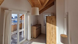 A high-ceilinged room with wooden beams, a sliding glass door leading outside, and a small wooden cabinet. - Chalet in Kotschach by Ski Slopes (Kotschach-Mauthen)