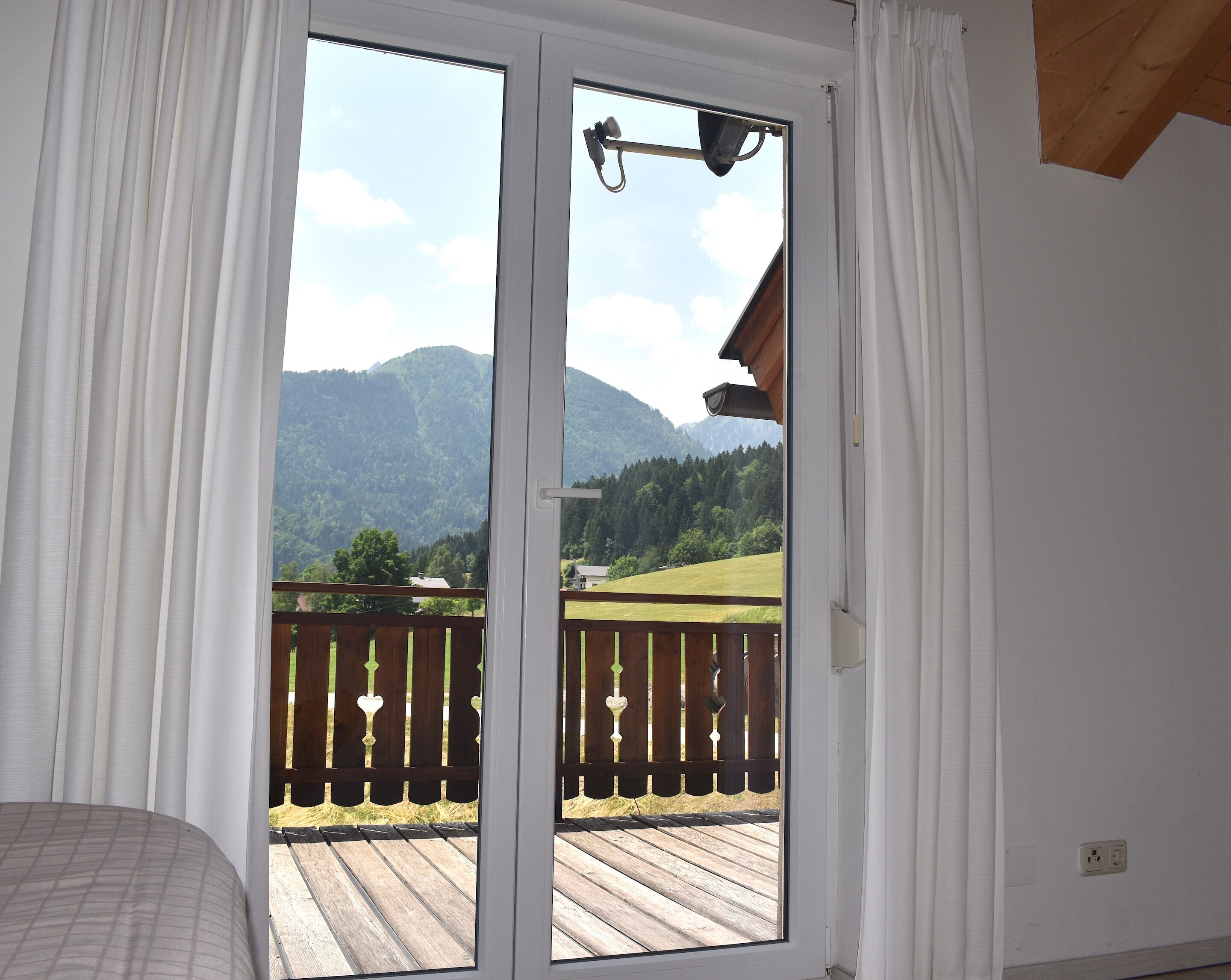Una habitación con puerta de cristal corrediza que da a un balcón con terraza de madera y vistas a las montañas.