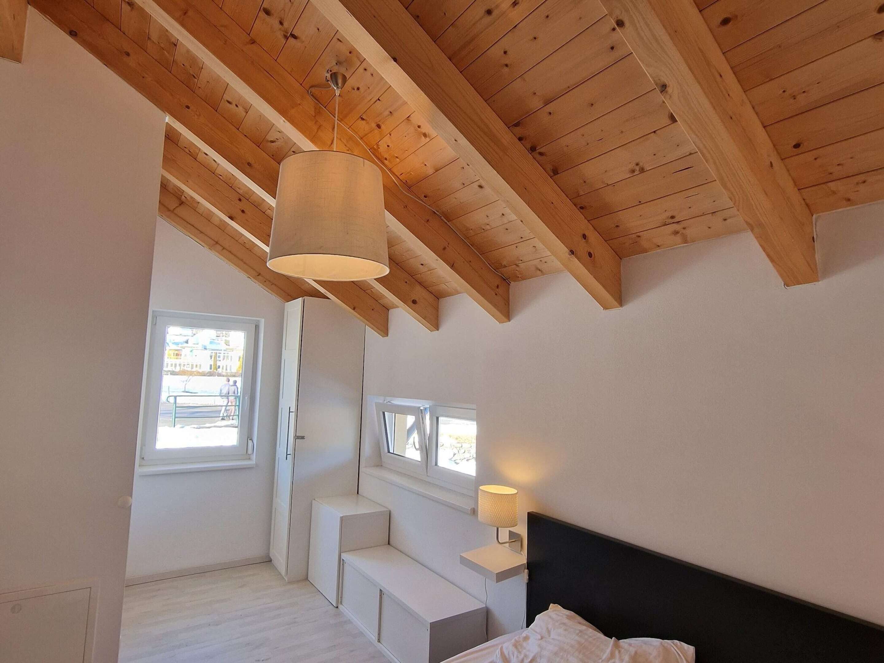 A bedroom with a sloped ceiling, built-in bench seating, a bed, and a bedside lamp.