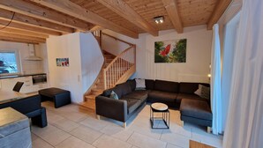 A modern living room with a wooden ceiling, a staircase, a kitchen area, and a large window. - Chalet in Kotschach by Ski Slopes (Kotschach-Mauthen)