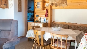 Een gezellige kamer met een houten plafond, een eettafel met stoelen, een bank en een keuken met kastjes en een hanglamp.