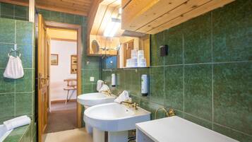 Un baño con dos lavamanos, un espejo y paredes con azulejos verdes.