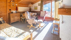 Een gezellig houten huisje met een bed, een eethoek en een stoel met kussen.