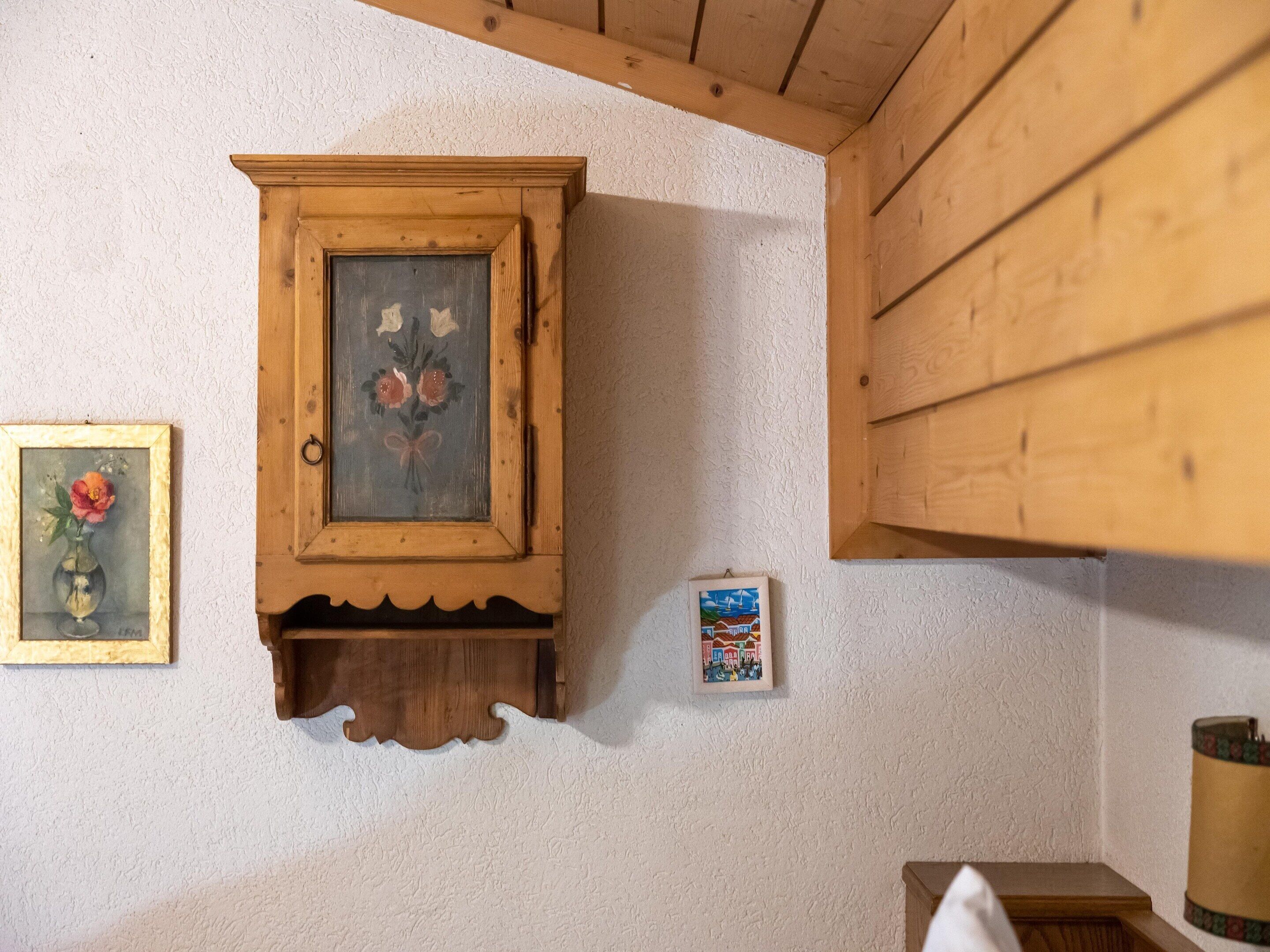 Un mueble de madera con una pintura floral, un cuadro pequeño enmarco y una repisa de madera.