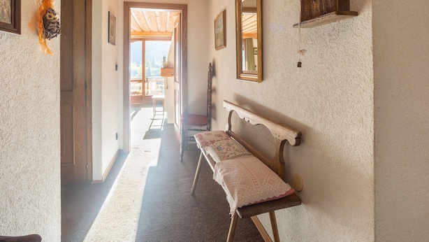 Een gang met een houten bankje, ingelijste foto’s en uitzicht op een buitenbalkon.