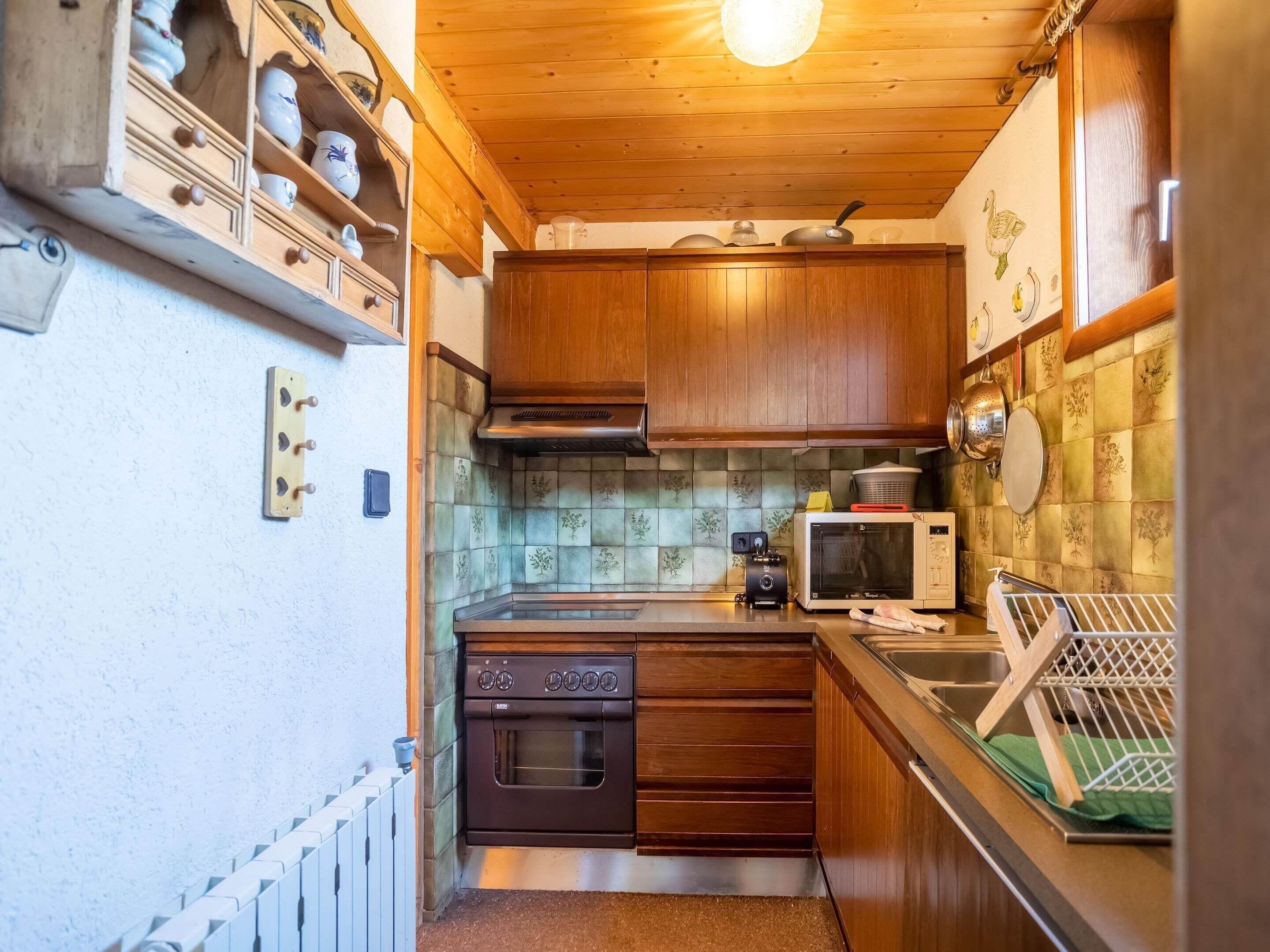 Une cuisine compacte avec des meubles en bois, un four encastré, un four à micro-ondes et un évier.