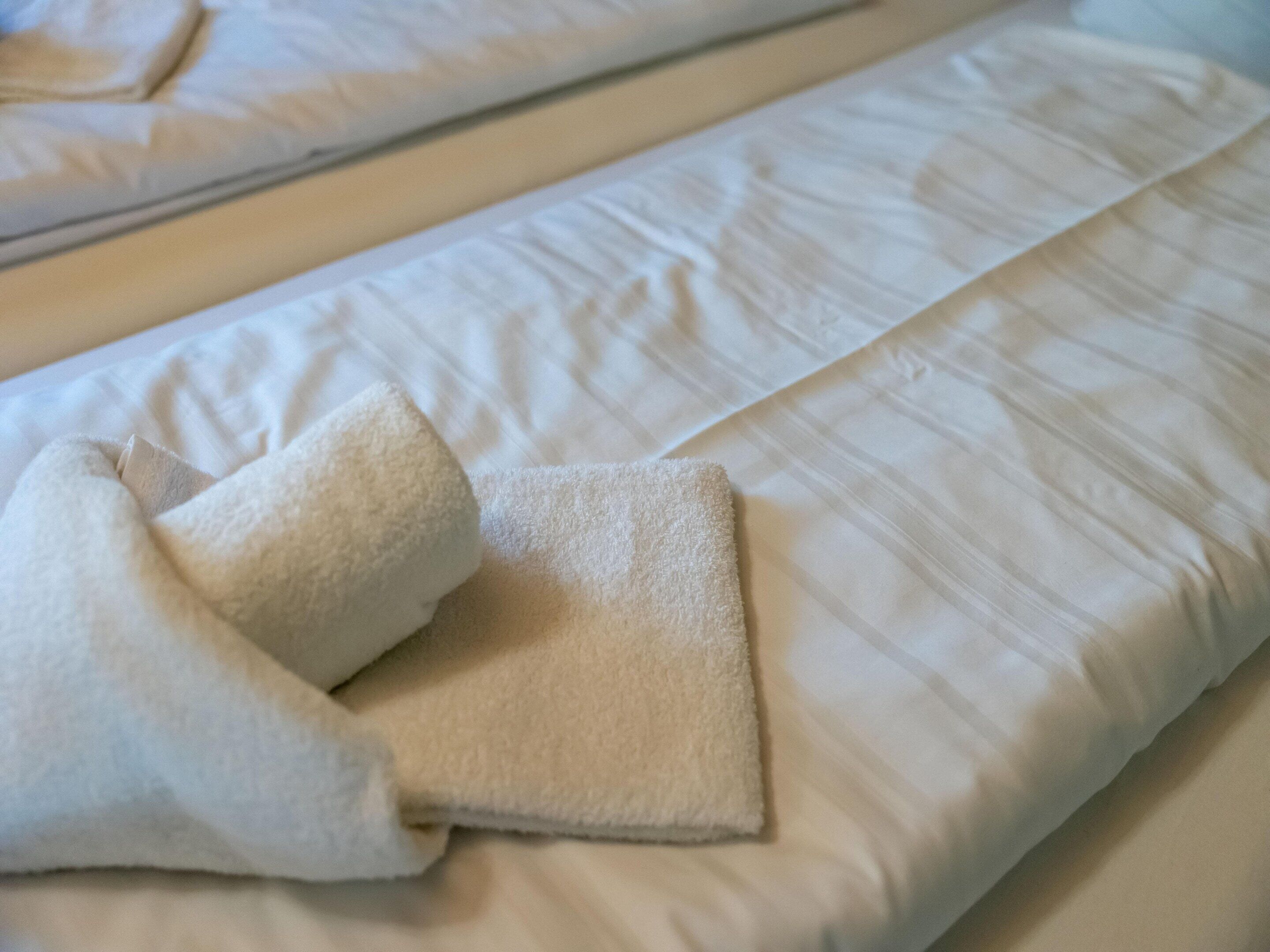 A neatly made bed with a white duvet and a folded towel on the side.