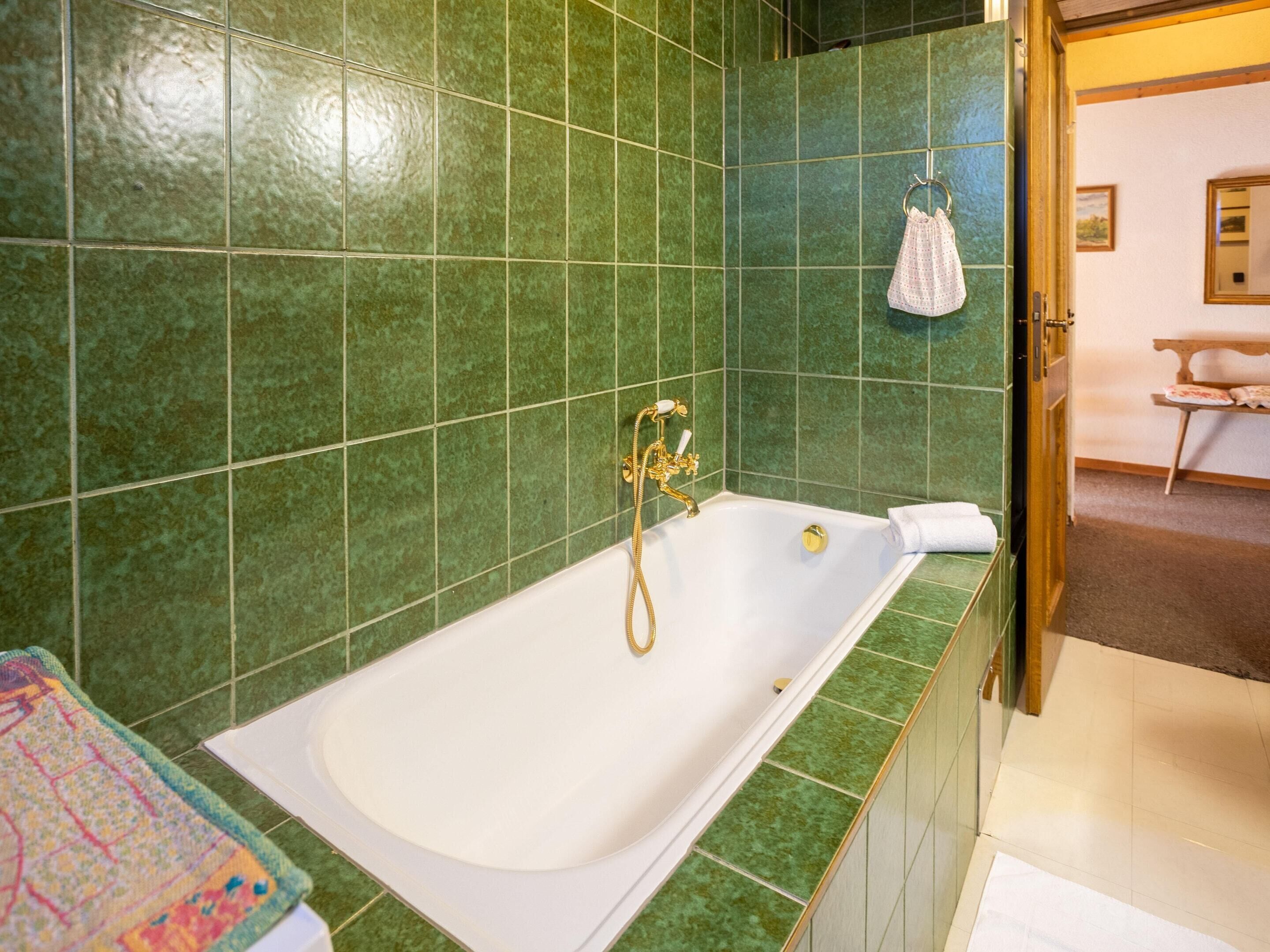 A bathroom with a large bathtub, green tiled walls, and a towel hanging on a hook.