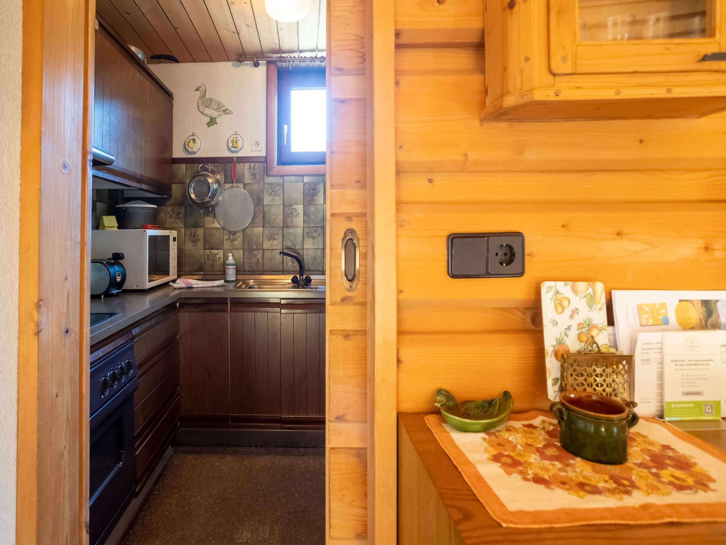 Una cocina compacta con armarios de madera, un microondas, una estufa y un lavabo. Hay una ventana sobre el lavabo y un estante pequeño con utensilios de cocina.
