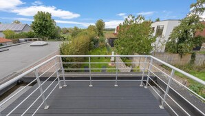Una terraza en la azotea con baranda de metal, vista del barrio circundante y cielo despejado.
