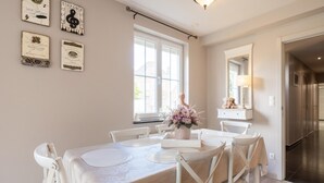 Un comedor con una mesa dispuesta para seis personas, sillas blancas, un florero con flores y certificados enmarcados en la pared.