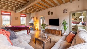 A spacious living room with a pool table, comfortable sofas, a wooden coffee table, and a TV.