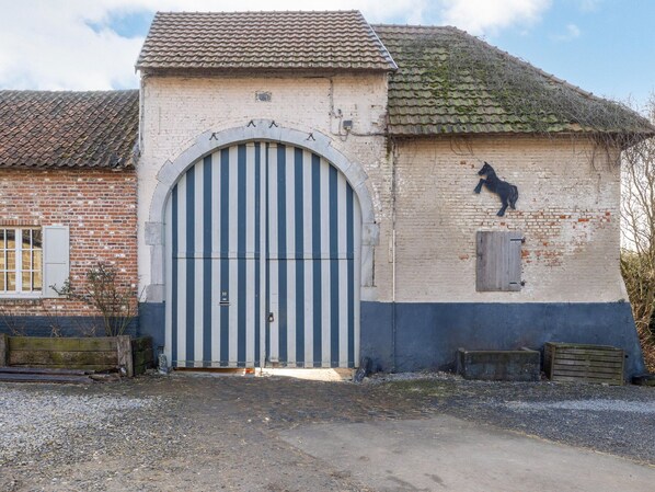 A building with a large arched entrance, a horse sculpture on the wall, and a brick facade. - Riding School Farm Stay (Sint-Truiden)