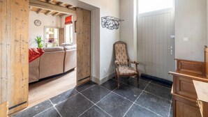 A room with a wooden ceiling, a black-tiled floor, a wooden chair, a door, and a view into another room with a sofa and a plant.
