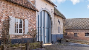 A brick building with a large arched entrance and a smaller door, surrounded by gravel and a wooden fence.