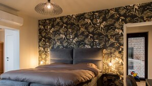 A bedroom with a large bed, a headboard, a nightstand, a lamp, and a wall with a tropical wallpaper. - Holiday Home in Vlijtingen With Sauna (Riemst)