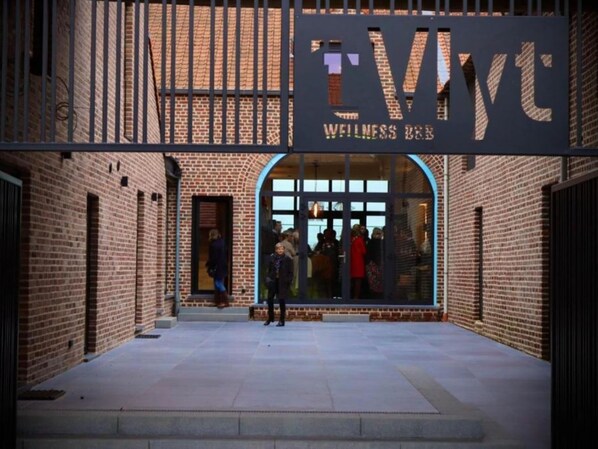 Een bakstenen gebouw met een grote gewelfde entree en een bord waarop 'TWYC WELLNESS B&B' staat.