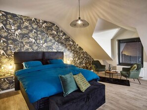 Een slaapkamer met een groot bed, een opvallend schuin dak en een tropisch behangdesign.