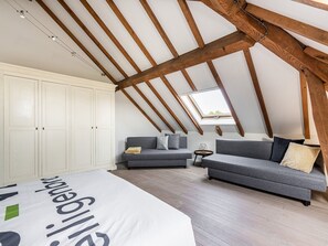 A loft bedroom with exposed wooden beams, a skylight, a grey sofa, a white wardrobe, and a bed with a large blanket. - Alken Farm Stay With Terrace (Alken)