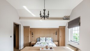 A spacious bedroom with a large wooden bed, a chandelier, and a window with a view of greenery. - Alken Farm Stay With Terrace (Alken)