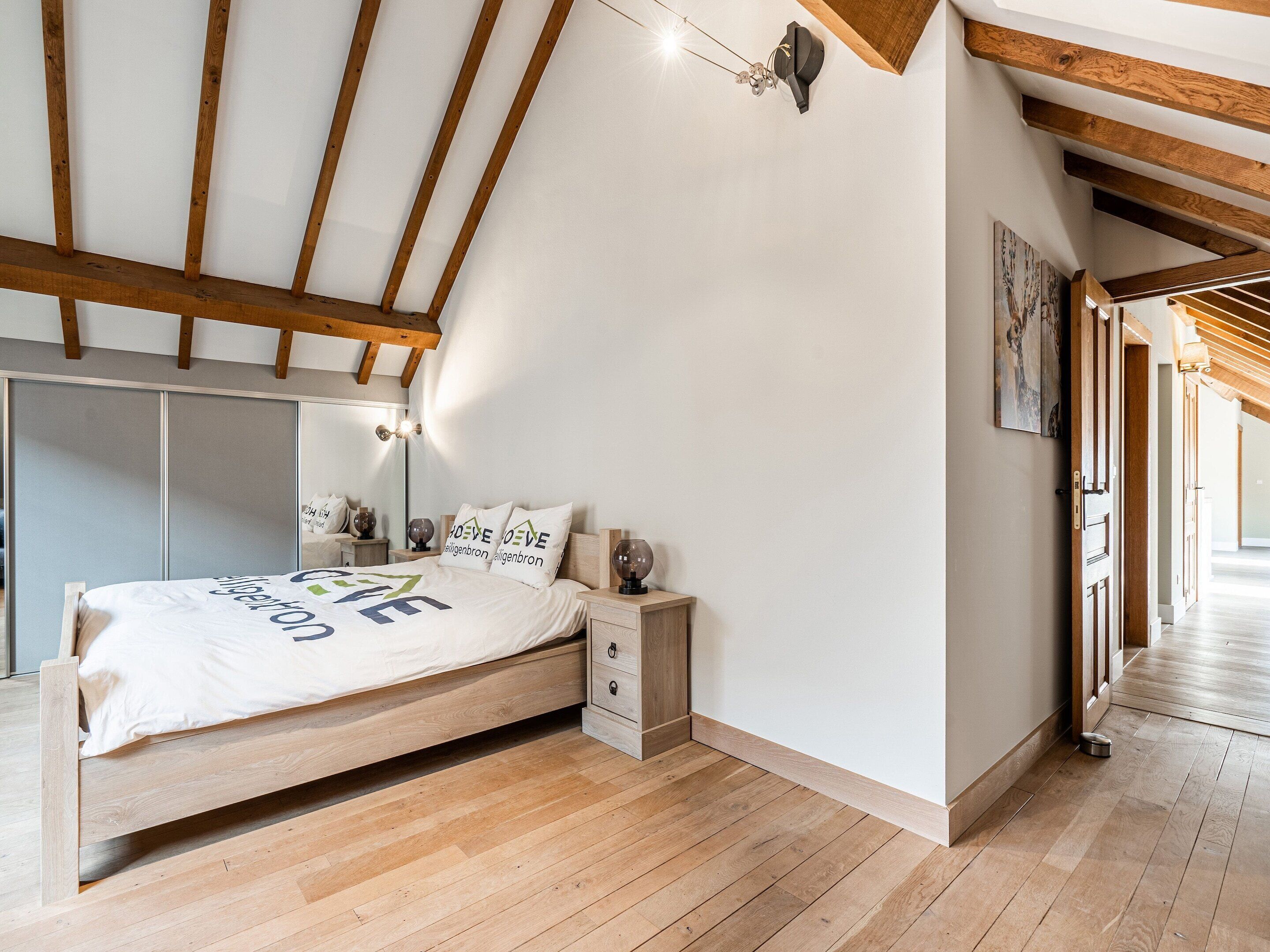 A bedroom with a wooden bed, a nightstand, a bedside table, and a wall-mounted light fixture.