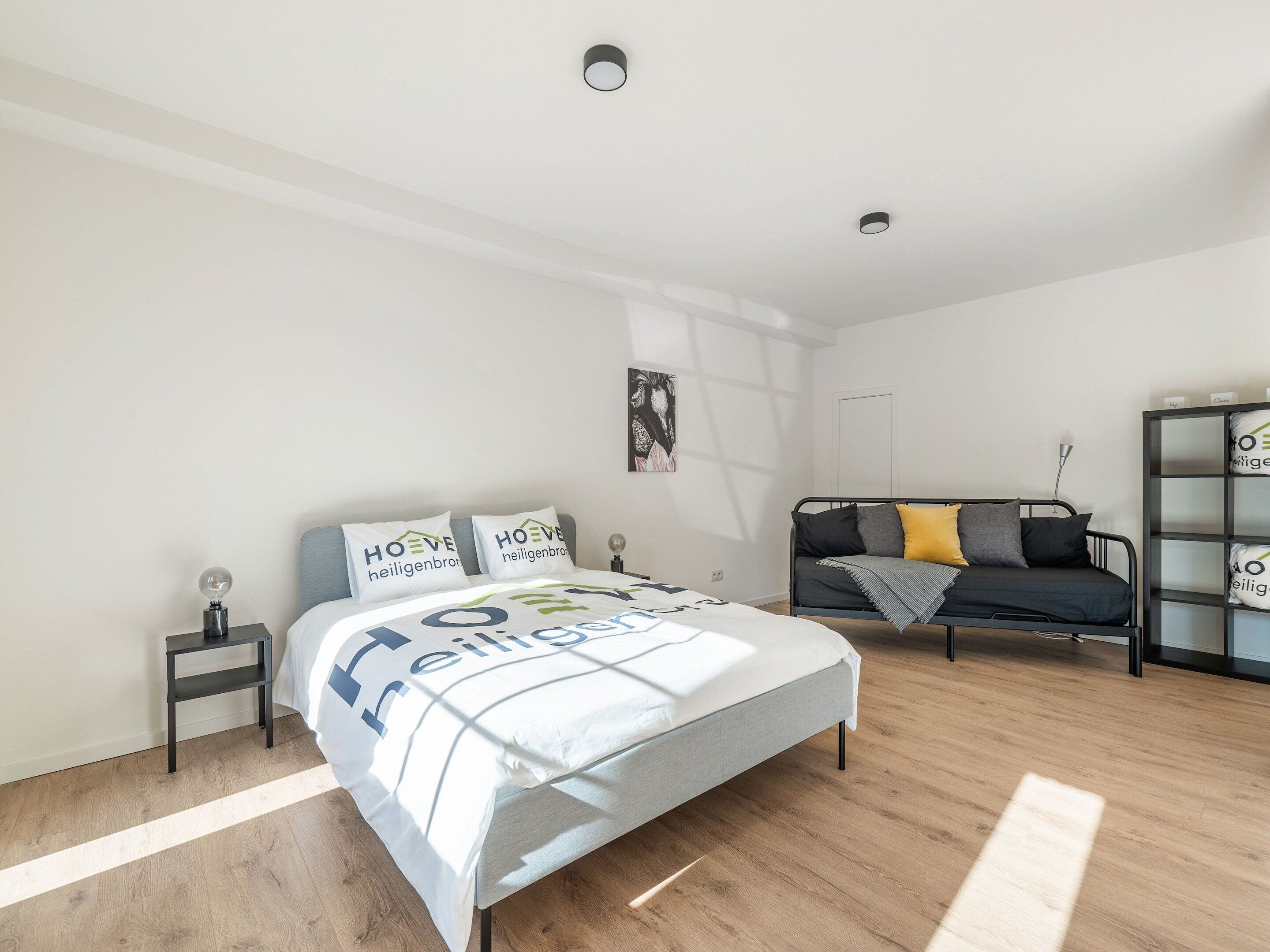 A modern bedroom with a bed, a sofa, and a bookshelf.