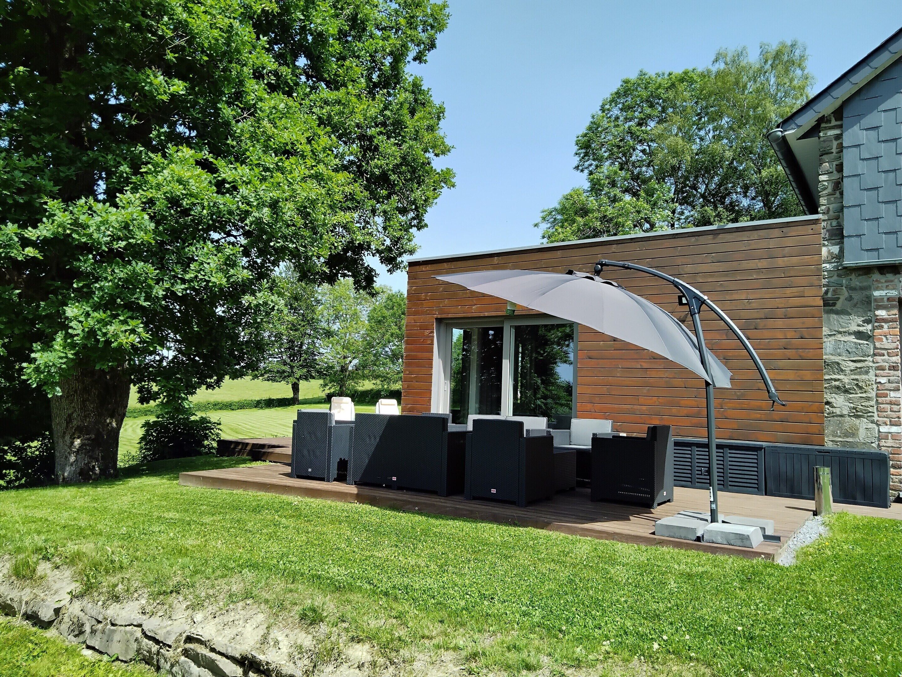 A modern outdoor seating area with a curved umbrella, a stone wall, and a wooden deck.