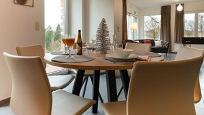 A dining area with a round table, chairs, a bottle of wine, and a Christmas tree. - Holiday Home in Waimes With Garden (Waimes)