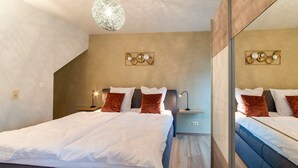 A modern bedroom with a large bed, a nightstand, a wall-mounted lamp, and a decorative wall piece. - Holiday Home in Waimes With Garden (Waimes)
