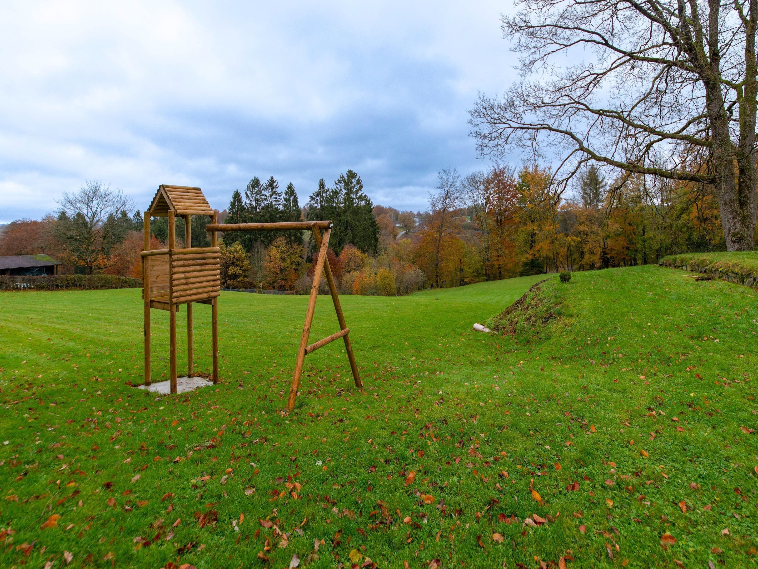A wooden swing set in a grassy field with trees in the background.