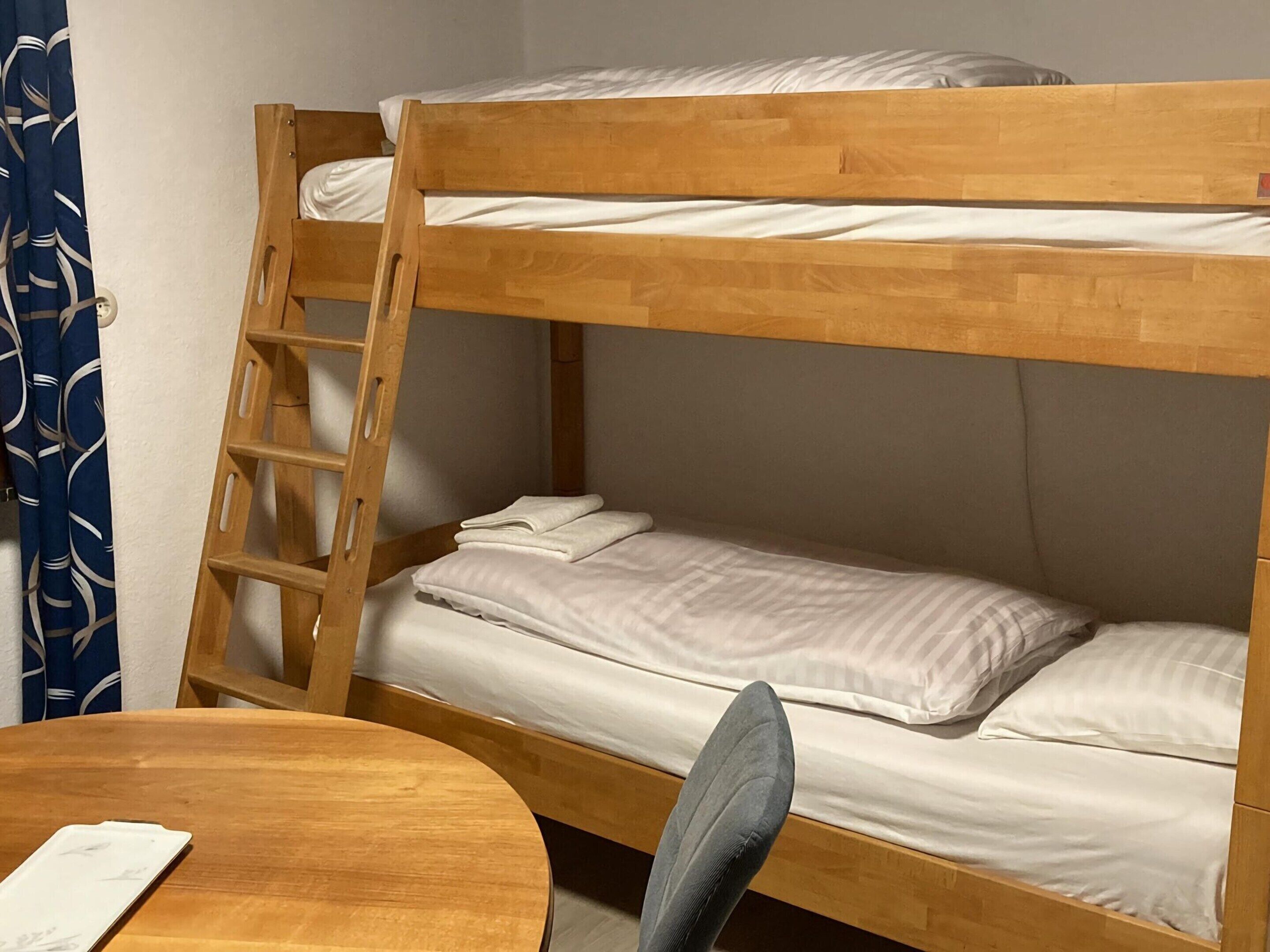 Una cama litera con escalera de madera, una mesa redonda de madera y una silla.