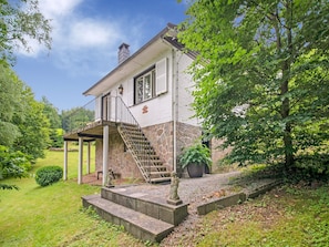 Une maison à deux étages, avec des fondations en pierre, un porche couvert et un escalier menant à l’étage supérieur.
